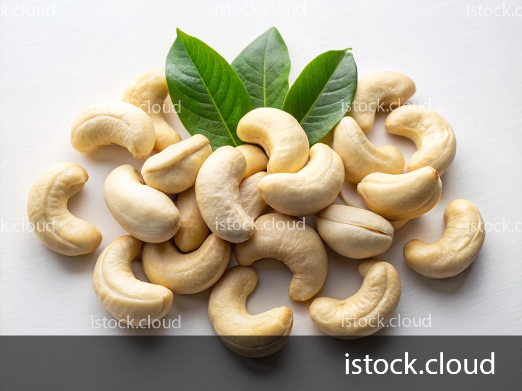 A cluster of raw cashew nuts accompanied by fresh green leaves, arranged on a white surface.