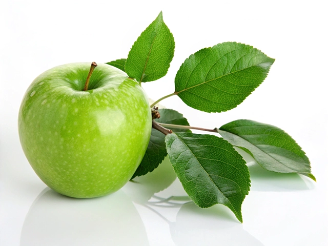A vibrant green apple resting on a reflective surface with a branch of green leaves.