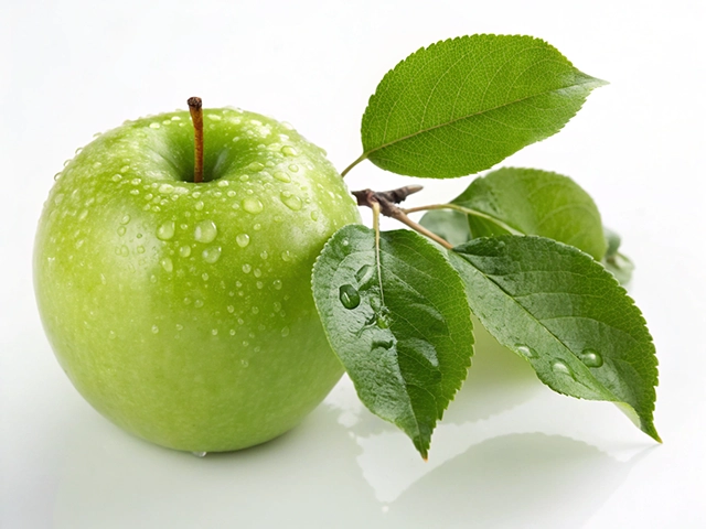 A fresh green apple with droplets of water on its surface, resting beside a branch with vibrant green leaves. The apple is placed on a clean white background, highlighting its freshness and dew.